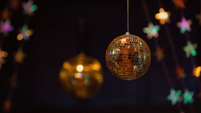 A golden mirror ball hangs from the ceiling surrounded by foil stars reflecting light from the surrounding fairy lights.